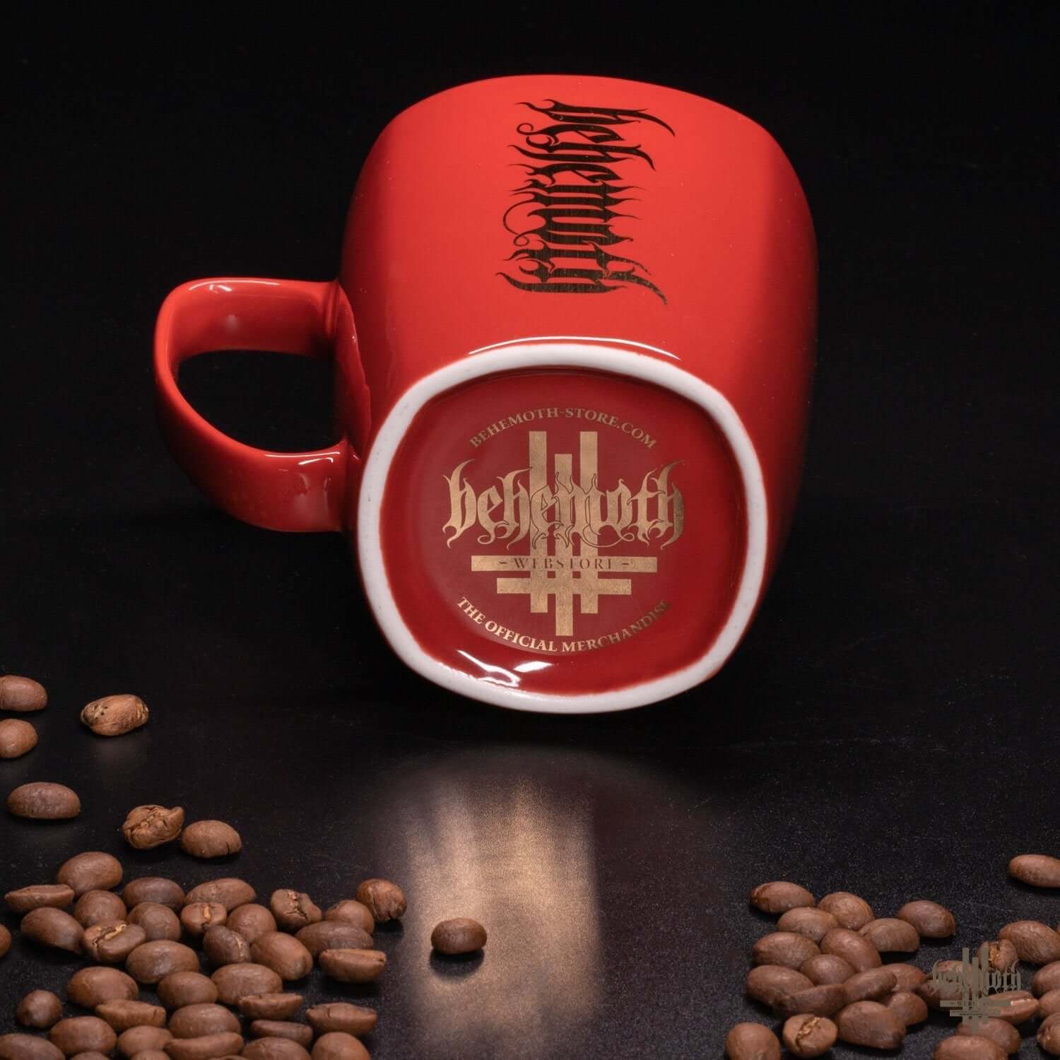 Red porcelain Behemoth mug with logo and coffee beans on a black surface.