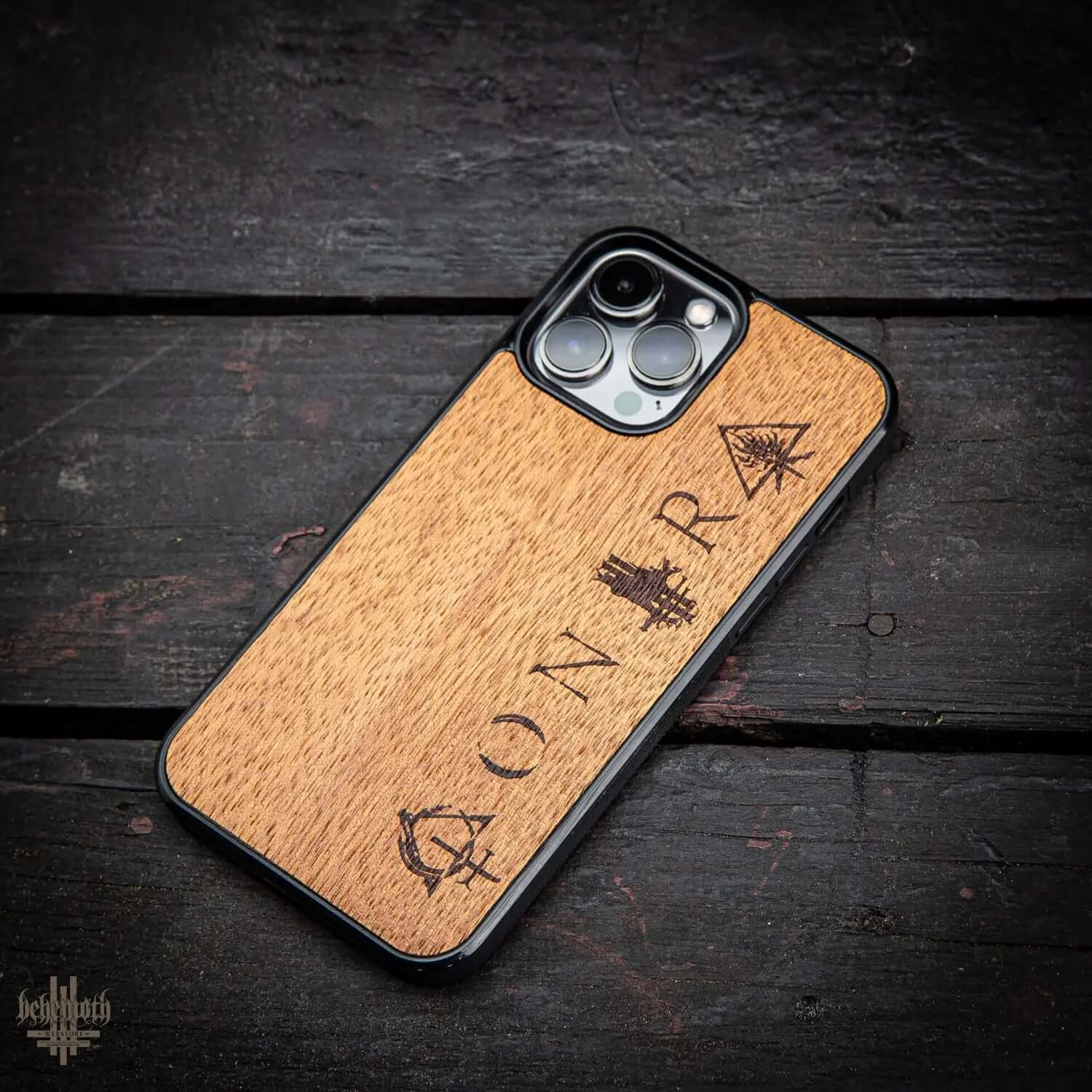 iPhone 13 Pro Max case with merbau wood finish and Behemoth CONTRA logo, made in Poland, on a dark wooden surface.