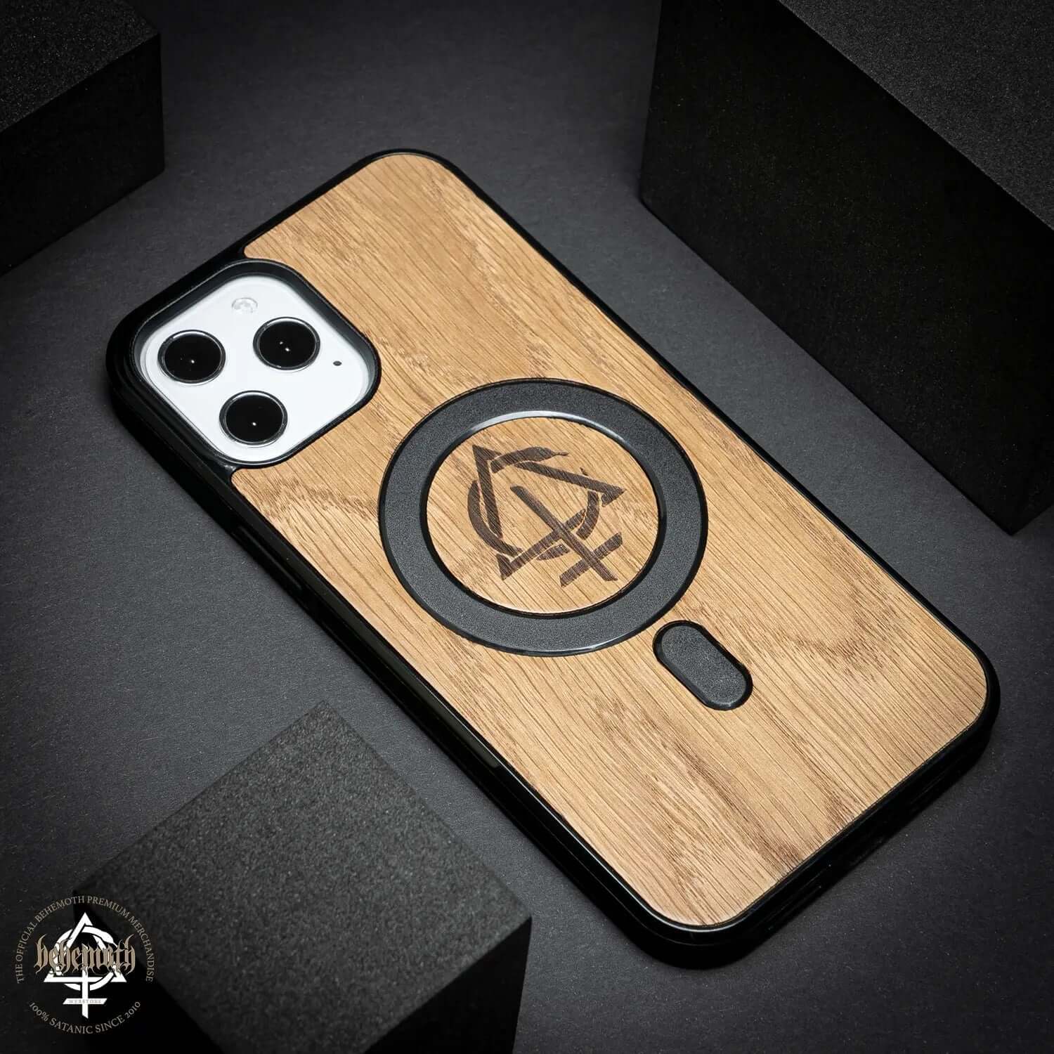 Apple iPhone 12 Pro Max case with oak wood finish and Behemoth 'CONTRA' logo, handcrafted in Poland.