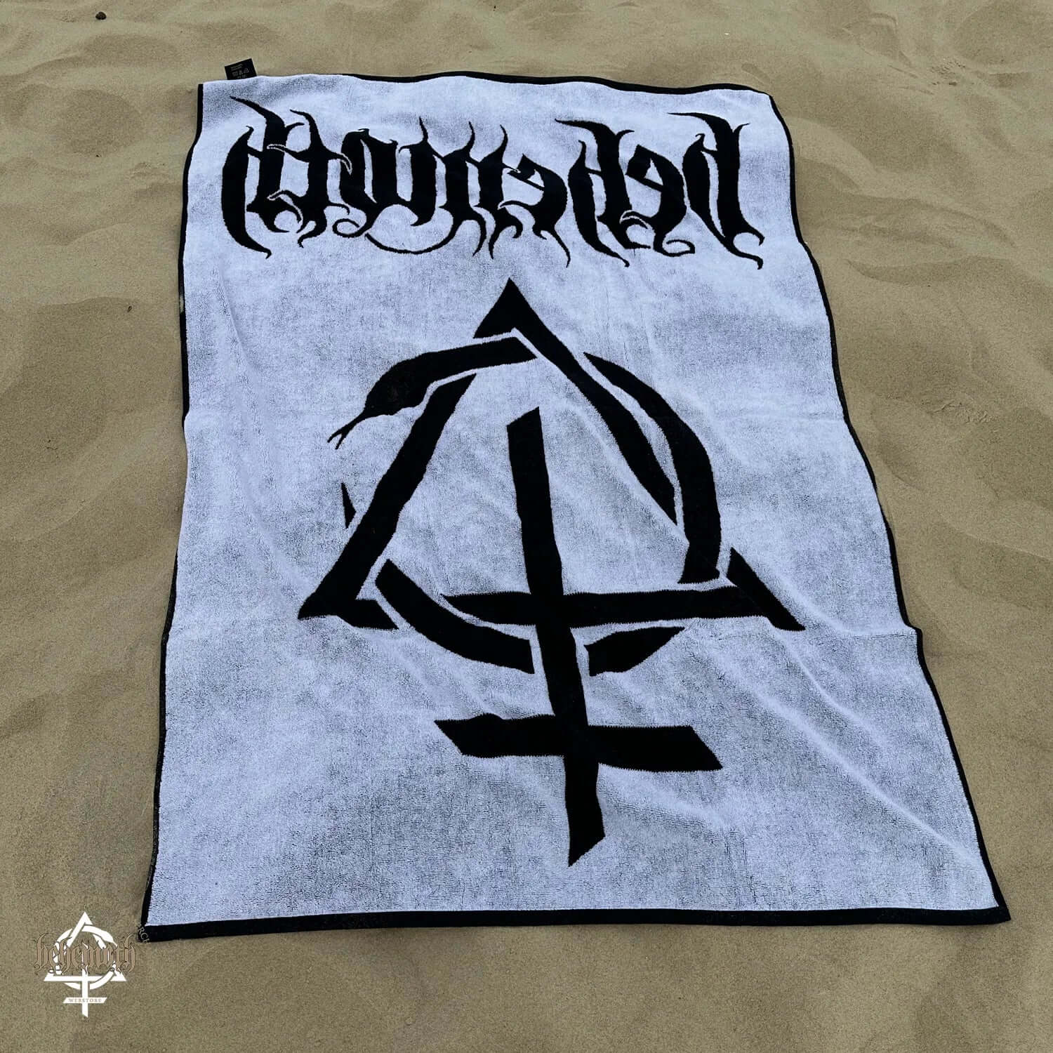 Behemoth 'Contra' 100% cotton woven towel on sand, featuring bold black graphic and text design.