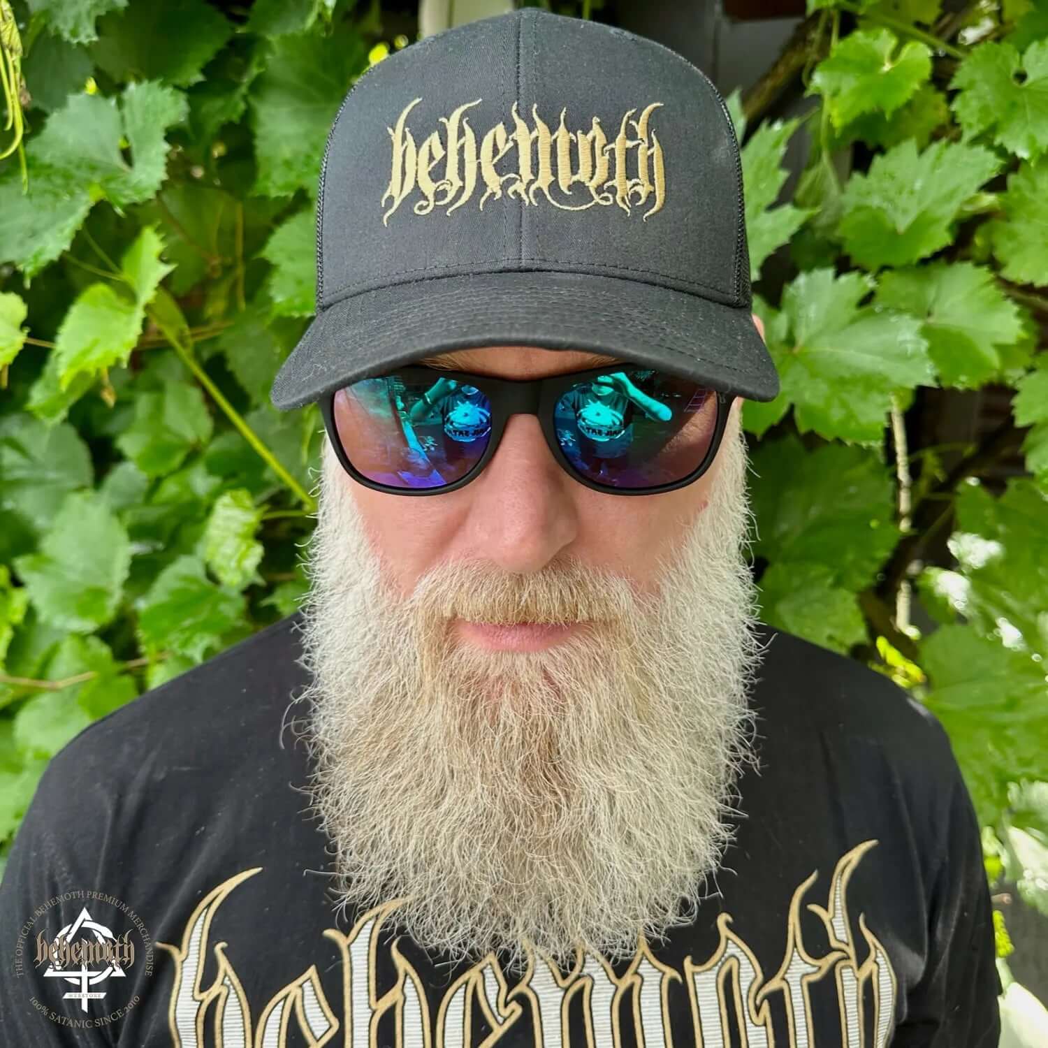 Man wearing Behemoth logo YP Classics® Retro Trucker Cap by Yupoong/Flexfit with beard and sunglasses, in outdoor setting.