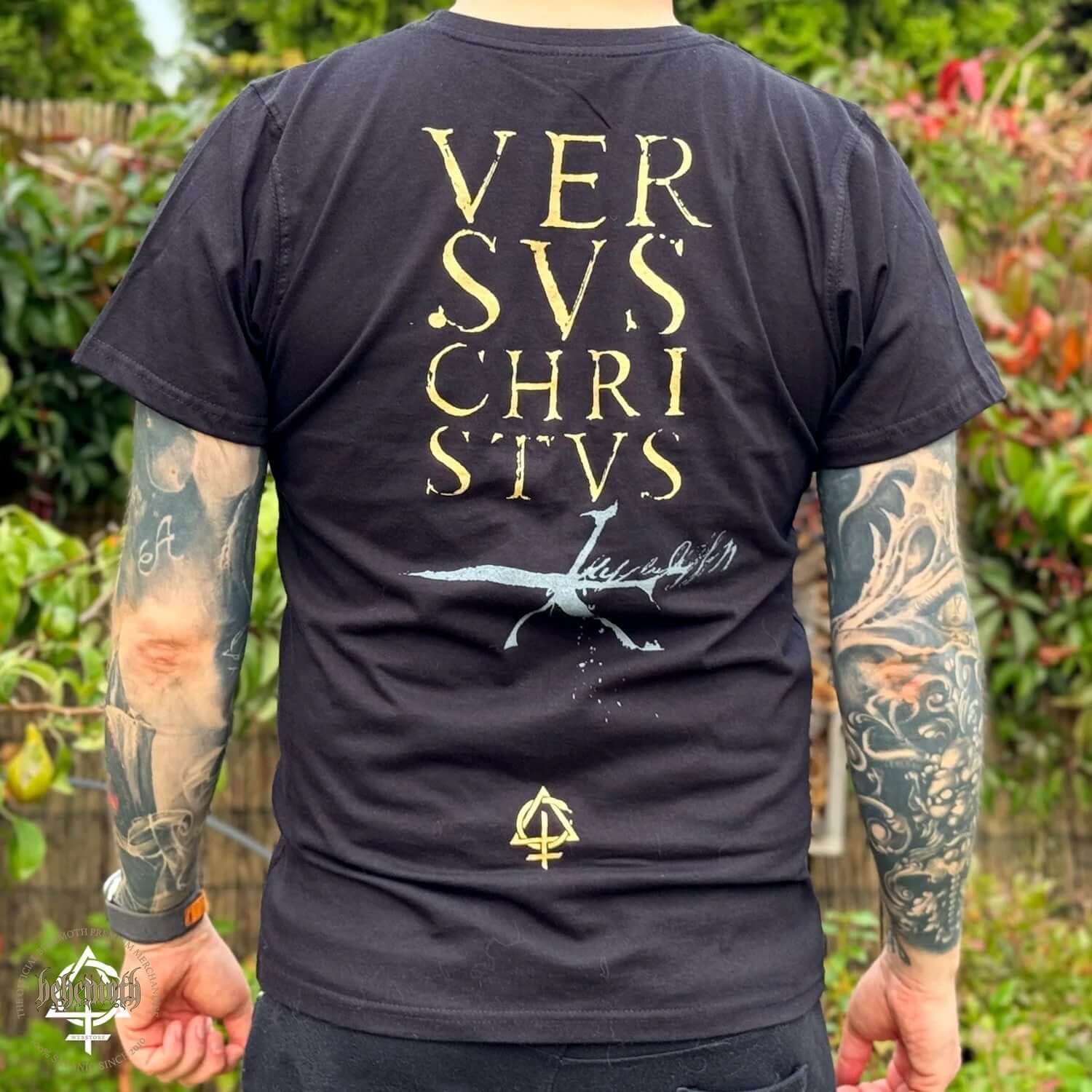 Back view of a tattooed person wearing a Versvs Christvs Behemoth T-shirt with front and back design, unisex, outdoor setting.
