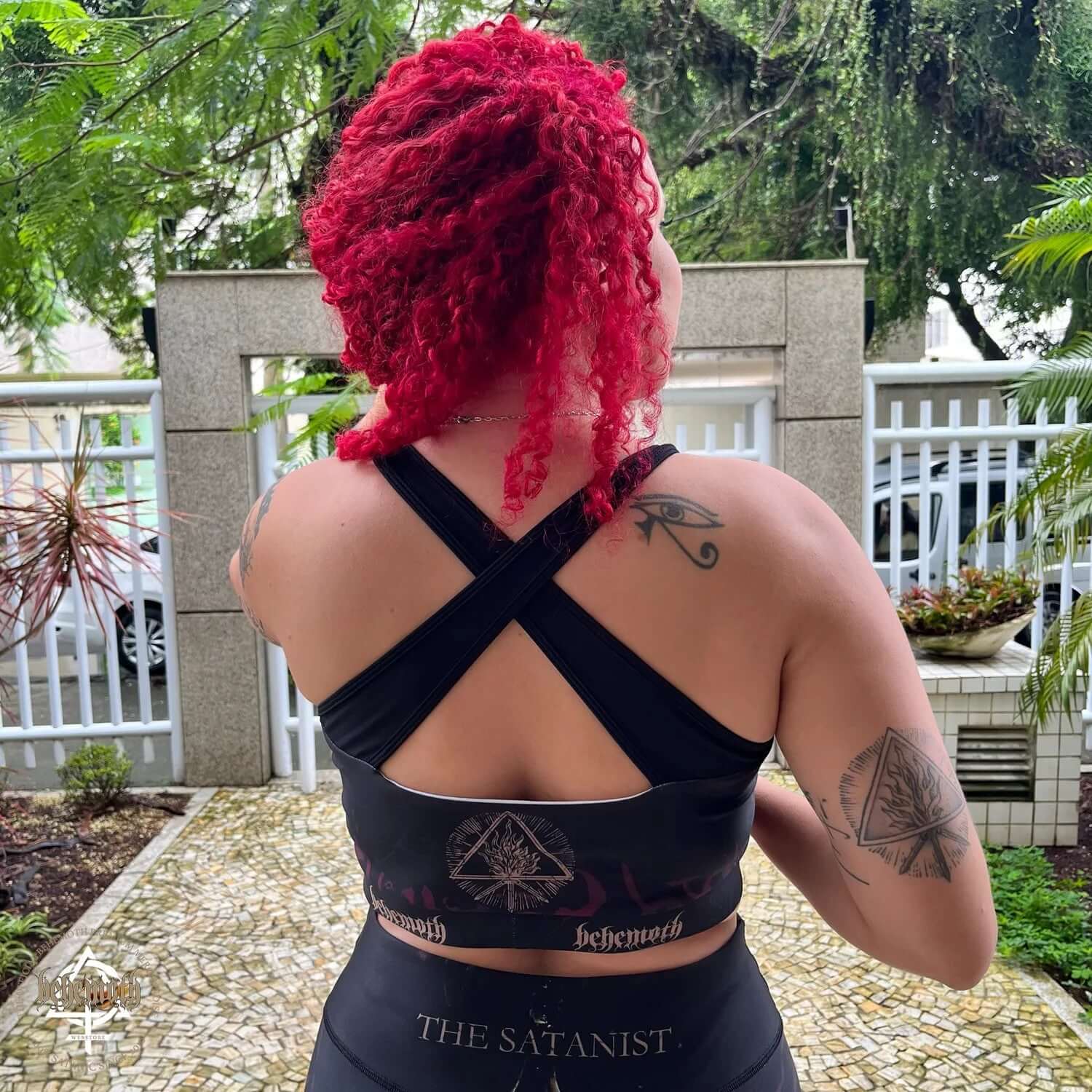 Back view of a woman wearing a Behemoth 'The Satanist' sports bra with intricate prints, showcasing unique crossback straps.