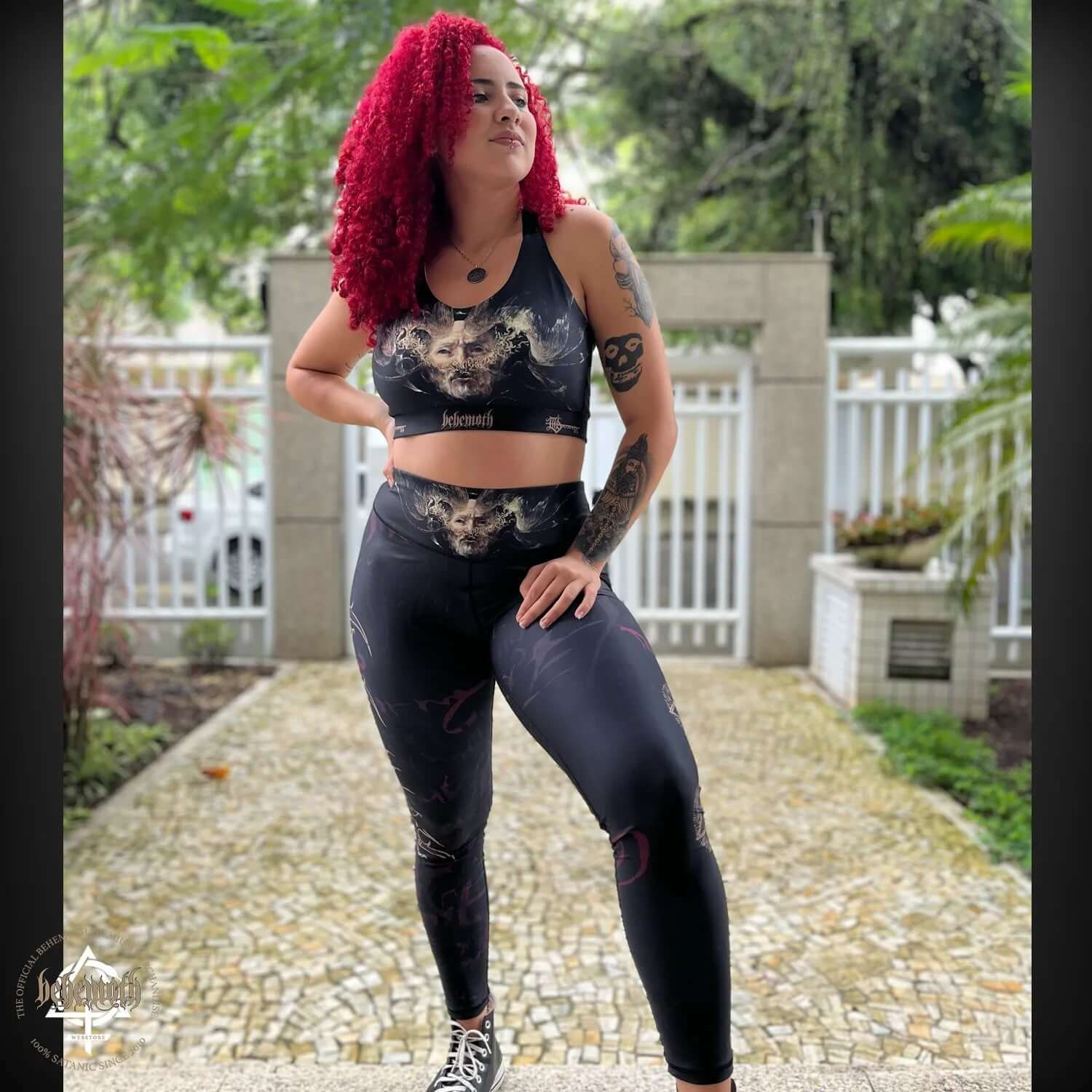 Woman wearing Behemoth 'The Satanist' sports bra and leggings, standing outdoors, showcasing gym and yoga wear fashion by Dani Batista.