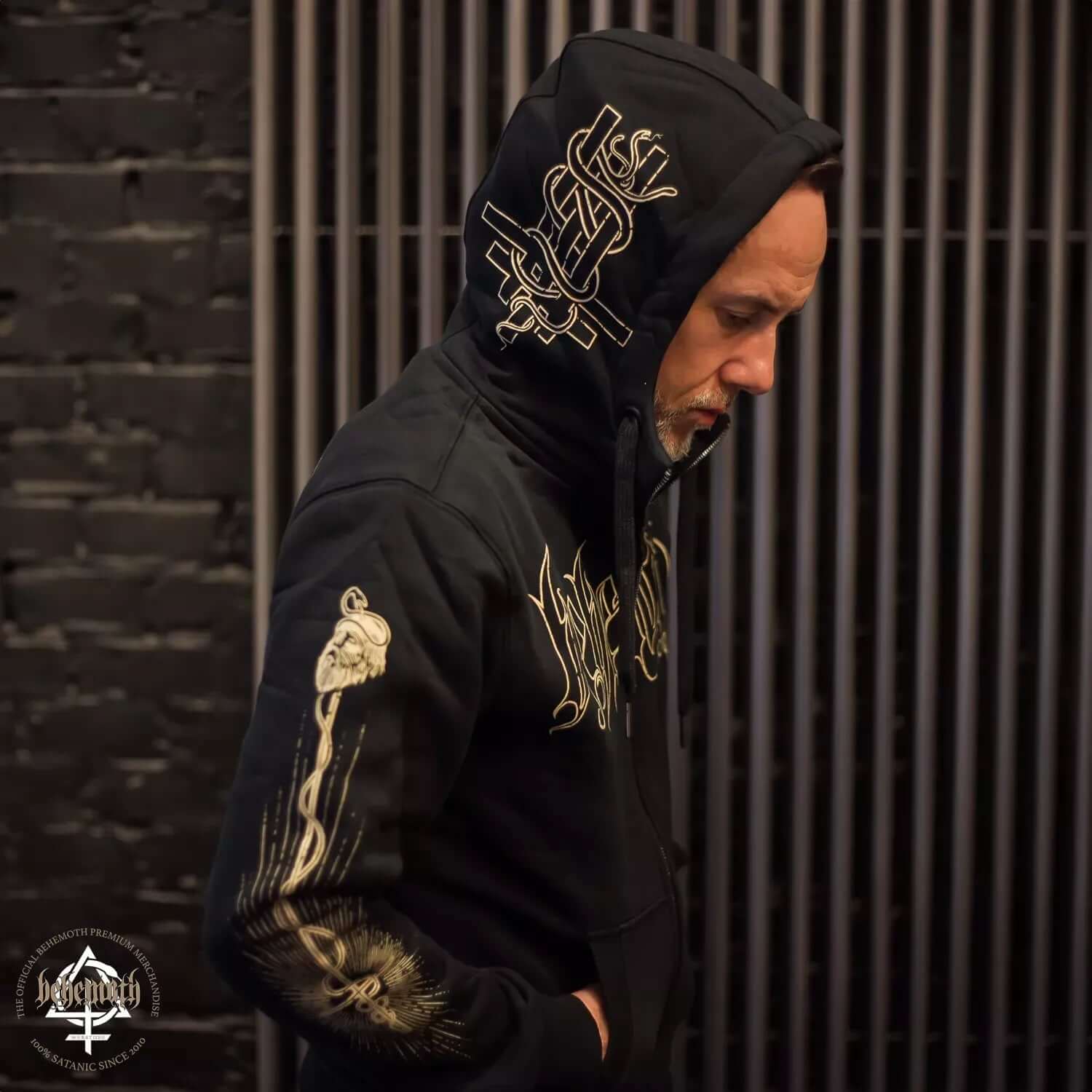 Man wearing Behemoth 'Adalbert' hooded sweatshirt with intricate sleeve and hood designs, showcasing premium unisex style and craftsmanship.