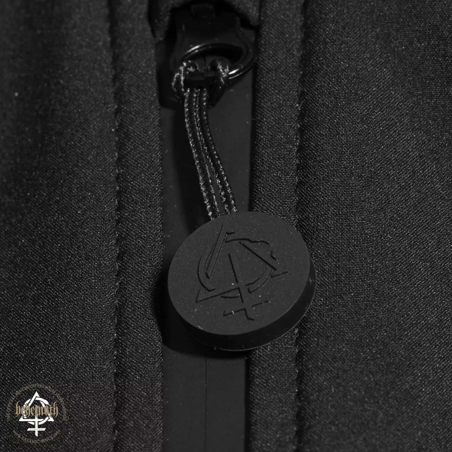Close-up of Behemoth Logo softshell jacket black zip puller with minimal branding emblem, part of the Blackest Ov The Black collection.