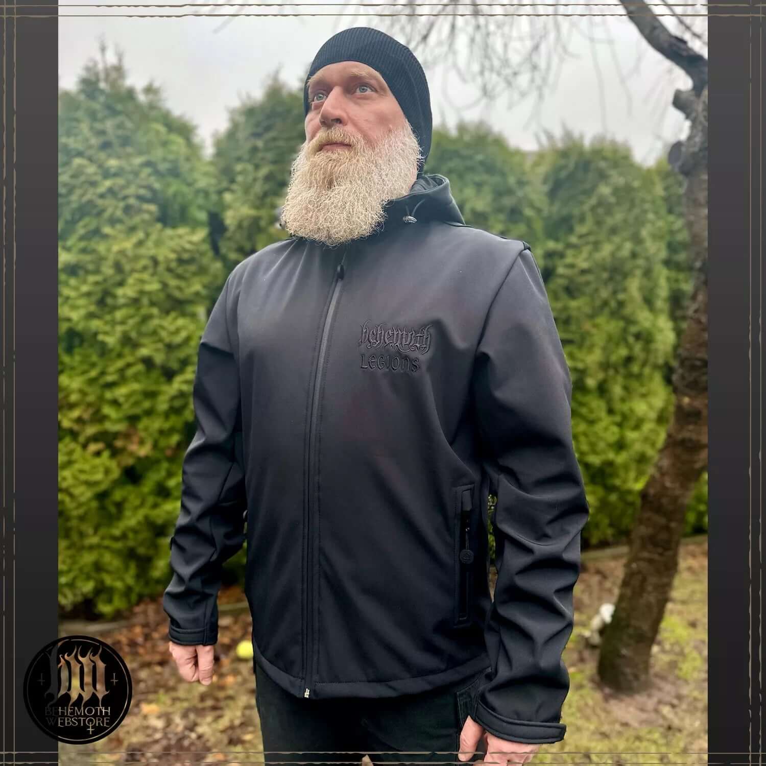 Man wearing Behemoth 'Legions' softshell jacket with embroidered logos, black on black, outdoors.