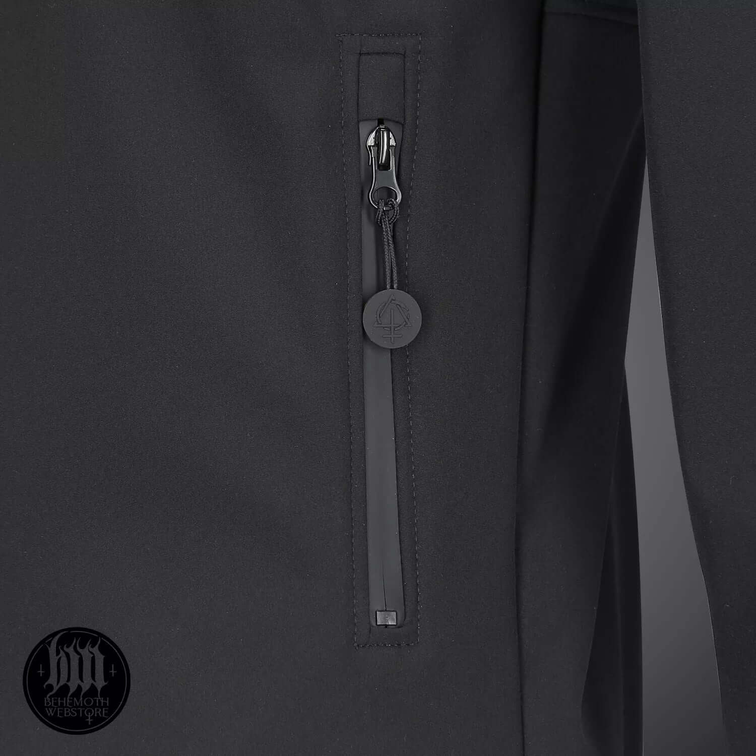 Close-up of Behemoth 'Legions' softshell jacket zip, featuring logo details and black zip puller.