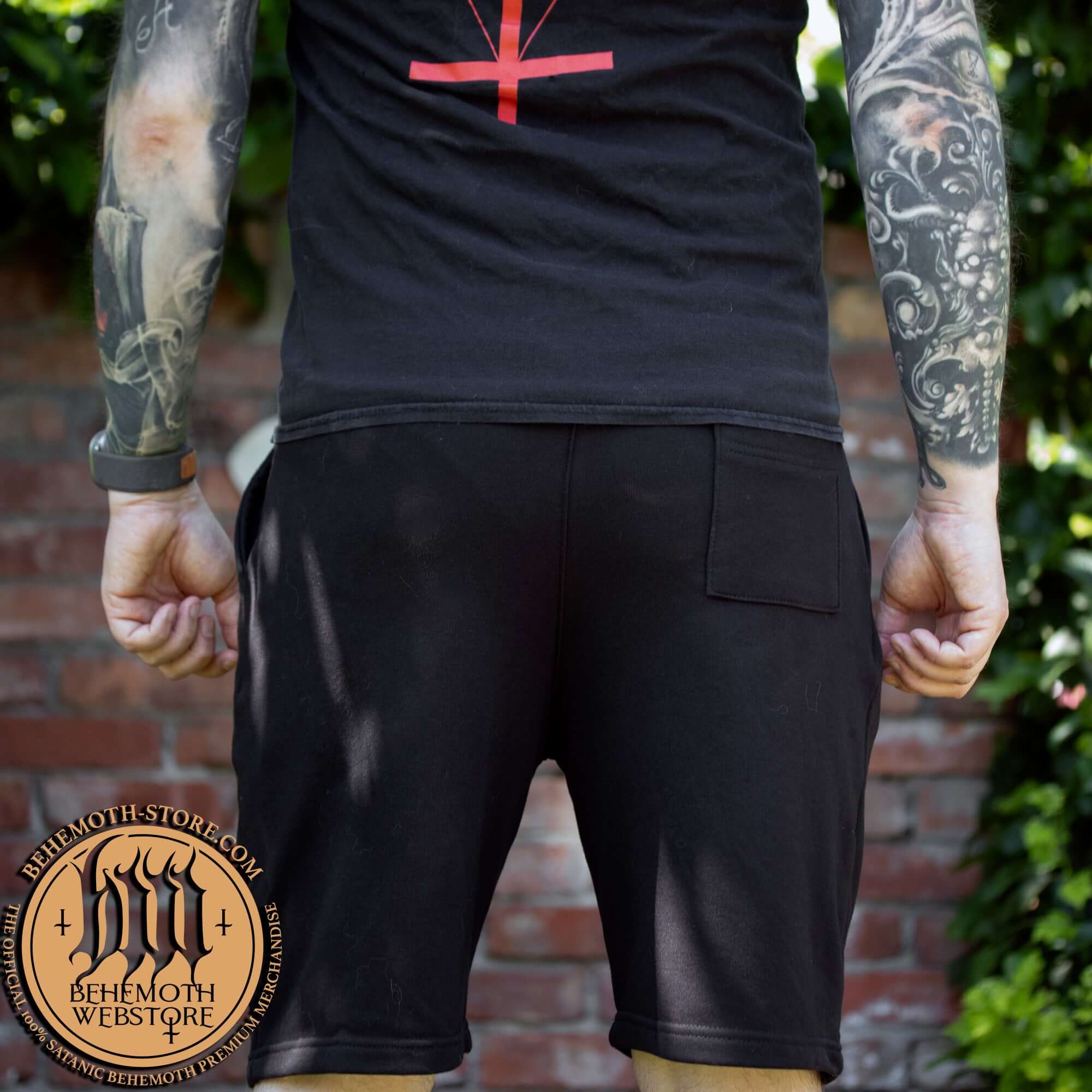 Person wearing Behemoth 'Absolvte Black' short sweatpants with back pocket, featuring bold design, outdoors in nature.
