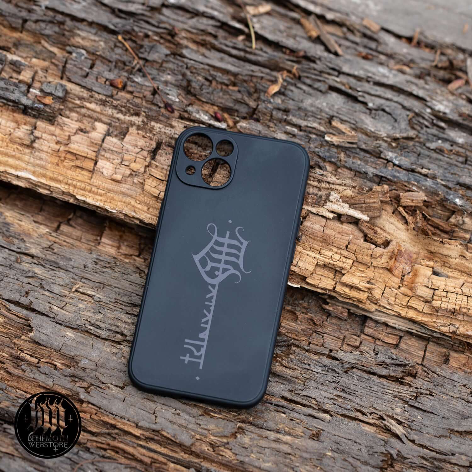 Behemoth 'The Satanist' black silicone phone case with Key Sigil design, protective and slip-resistant, lying on textured wood surface.