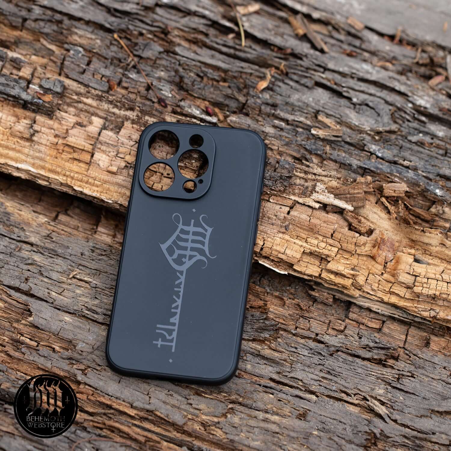 Behemoth 'The Satanist' phone case with black matte finish, featuring glossy key sigil design, resting on rustic wood surface.