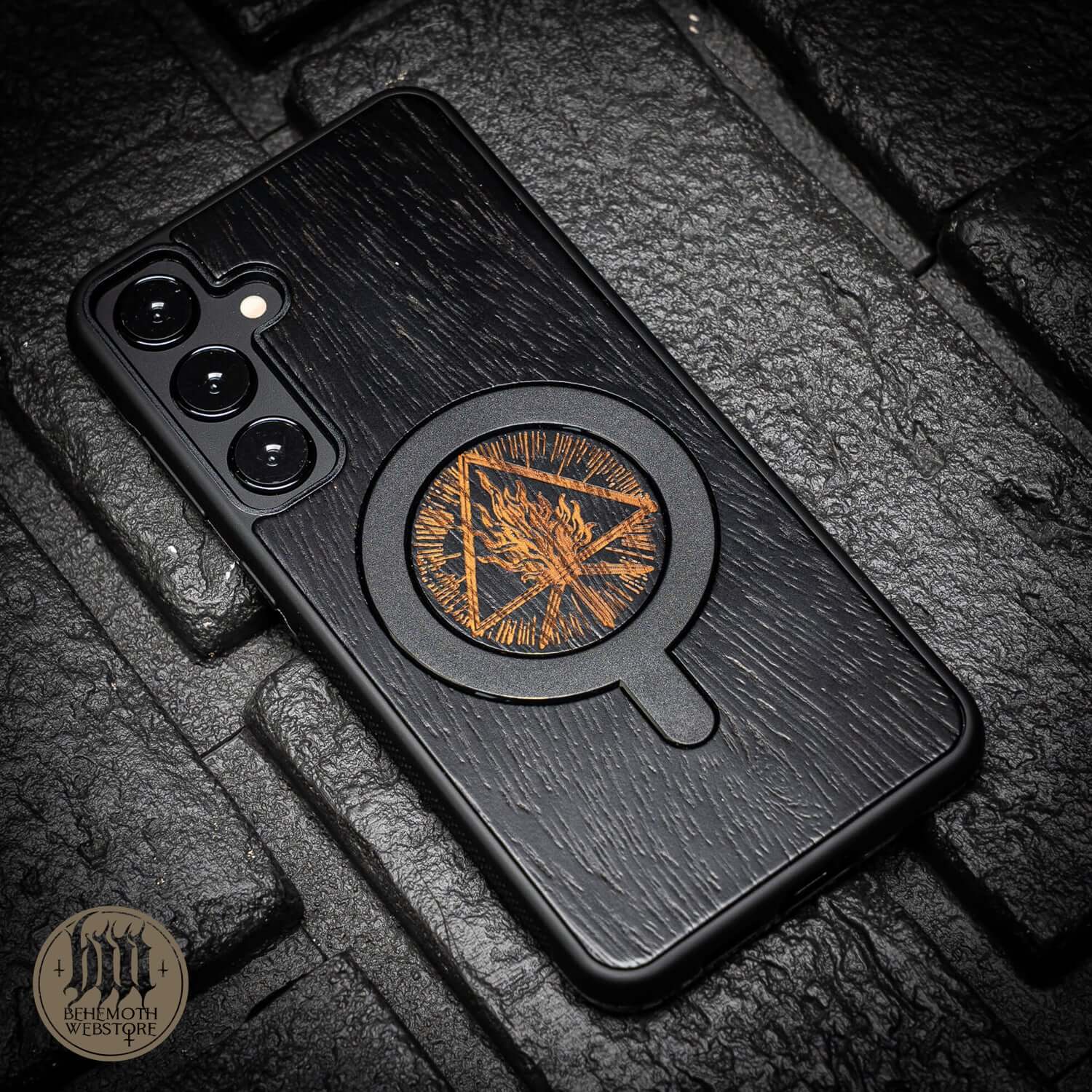 Behemoth 'Thru Fire We Walk' black oak wood TPU MagSafe phone case on textured surface.