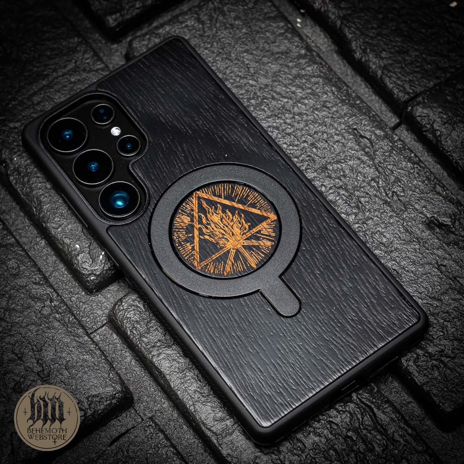 Behemoth 'Thru Fire We Walk' black oak MagSafe phone case on stone surface, featuring intricate design; made in Poland, hand-finished.