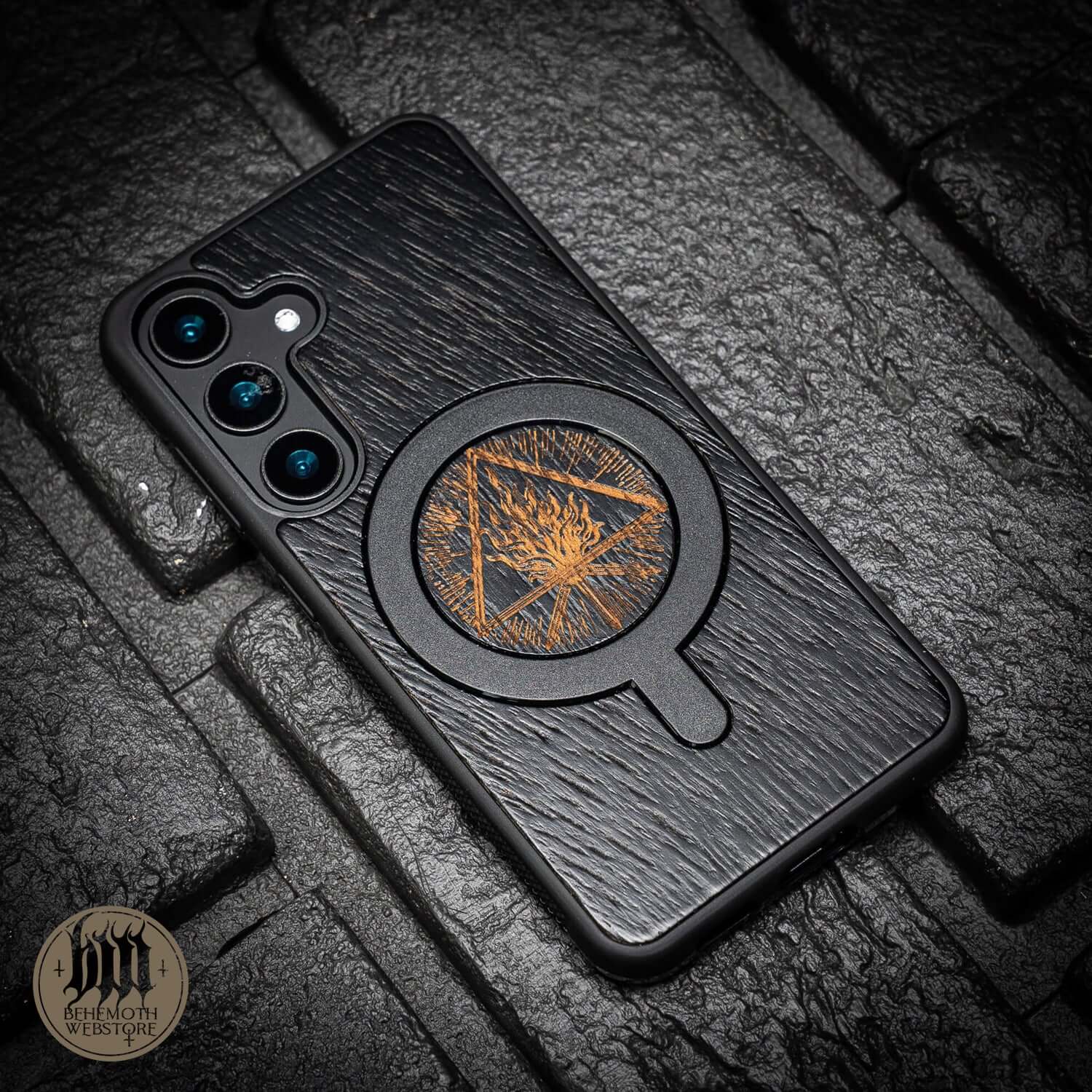Behemoth 'Thru Fire We Walk' black oak MagSafe phone case on stone background.