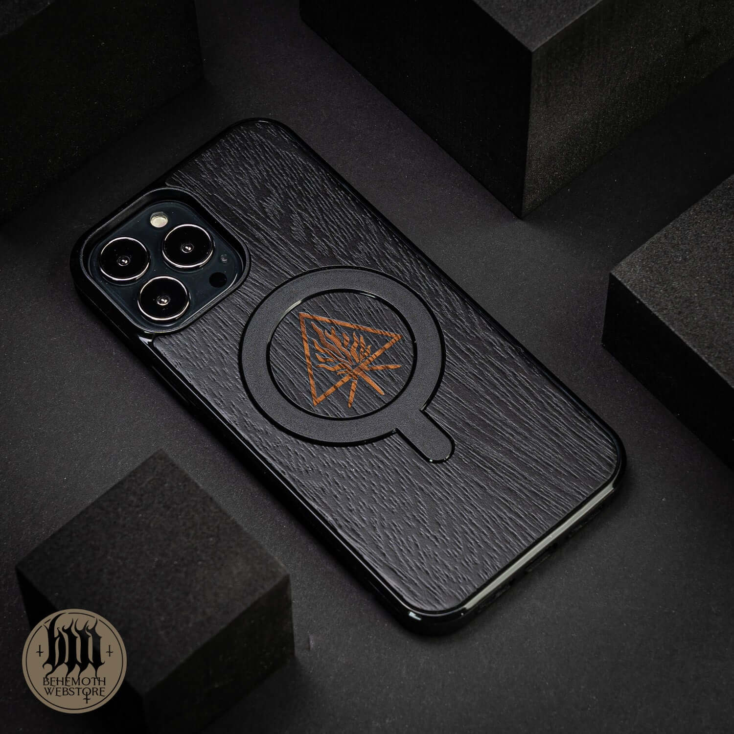 Behemoth 'The Unholy Trinity' black oak MagSafe phone case with silicone TPU, handcrafted in Poland, on a dark background.