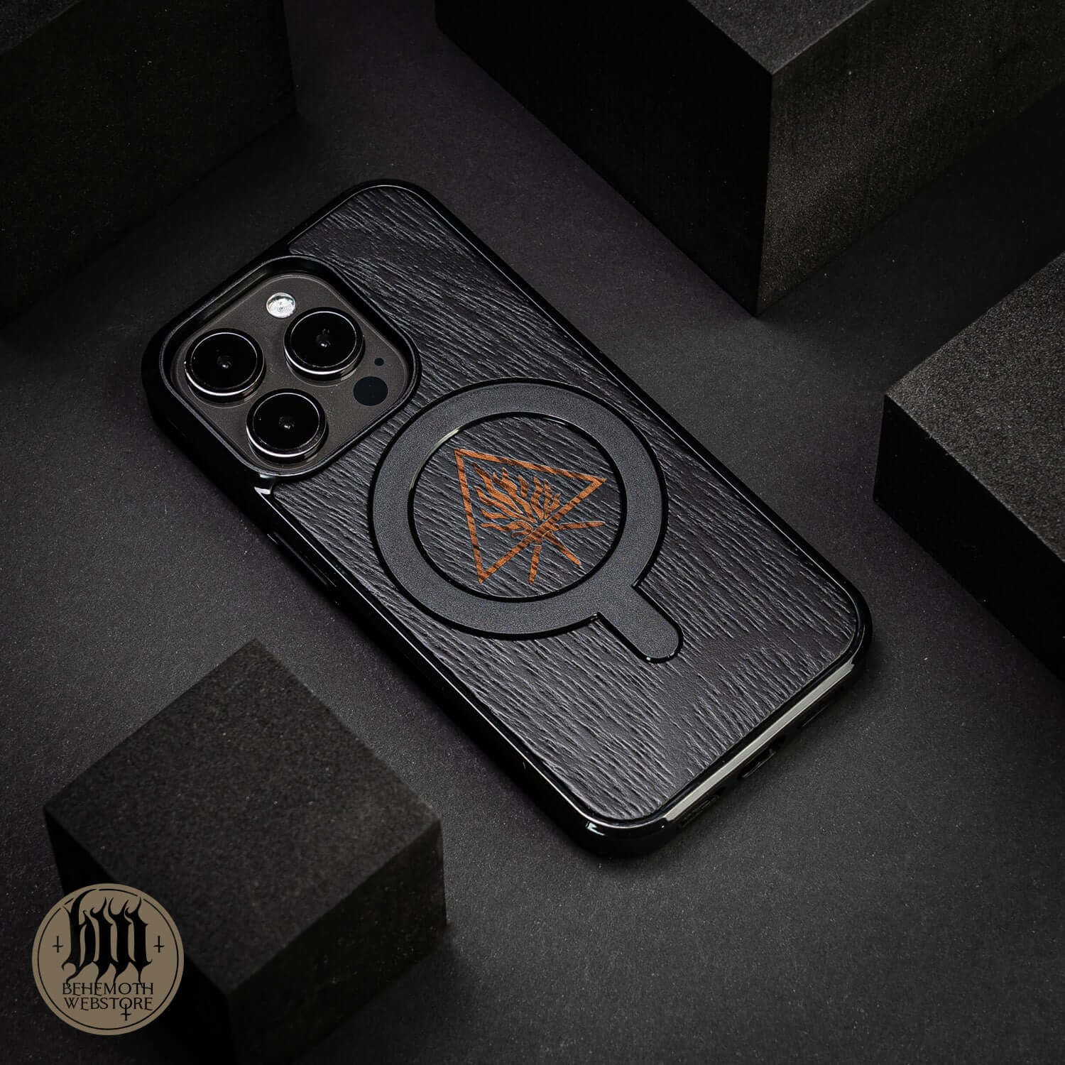 Behemoth 'The Unholy Trinity' black oak wood MagSafe phone case, hand-finished, shown on dark surface background.