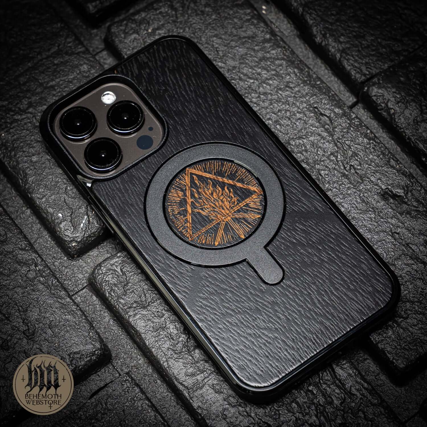 Behemoth 'Thru Fire We Walk' black oak MagSafe phone case on textured surface, featuring precision hand-finished design, made in Poland.