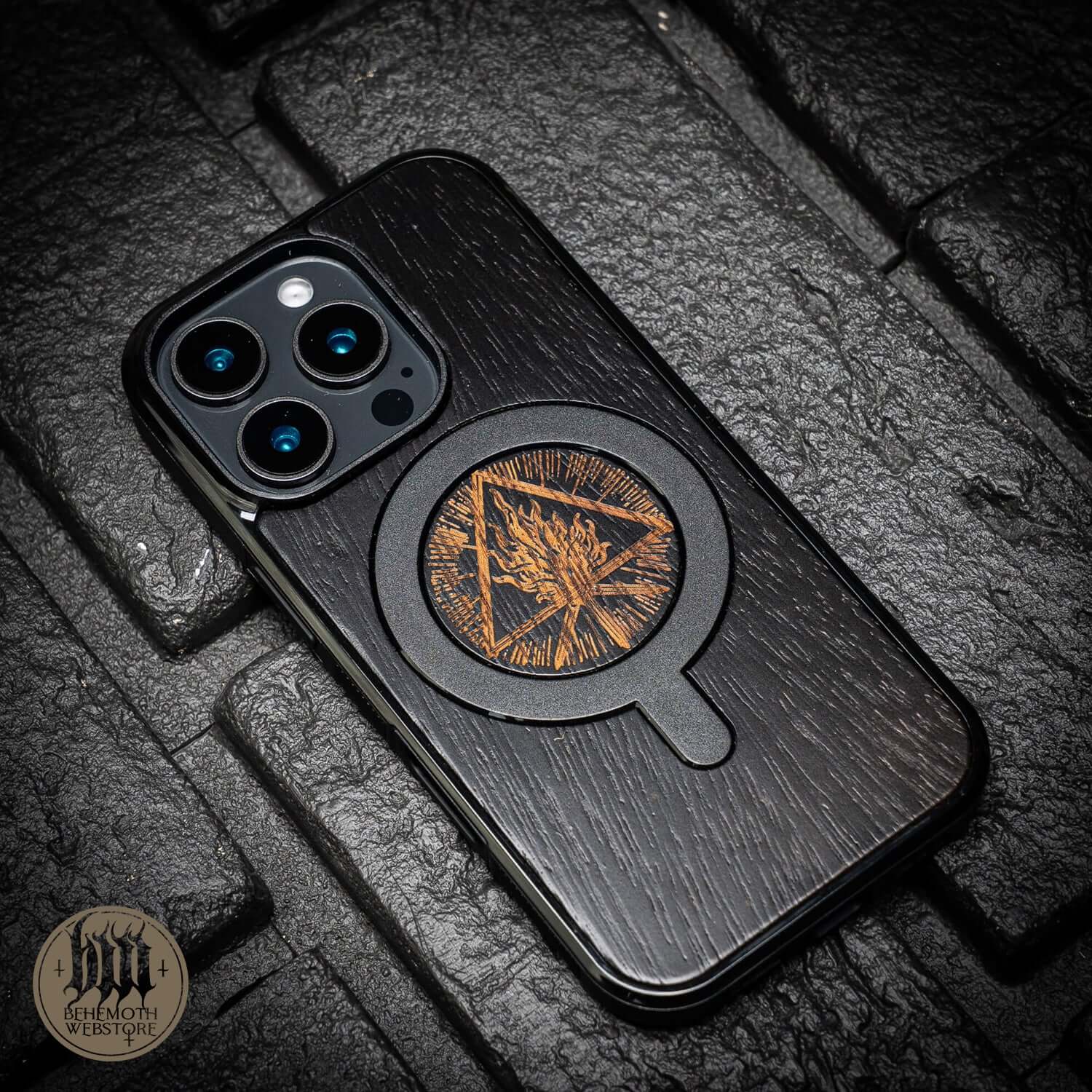 Behemoth 'Thru Fire We Walk' MagSafe phone case in black oak wood and silicone TPU, shown on a textured black surface.