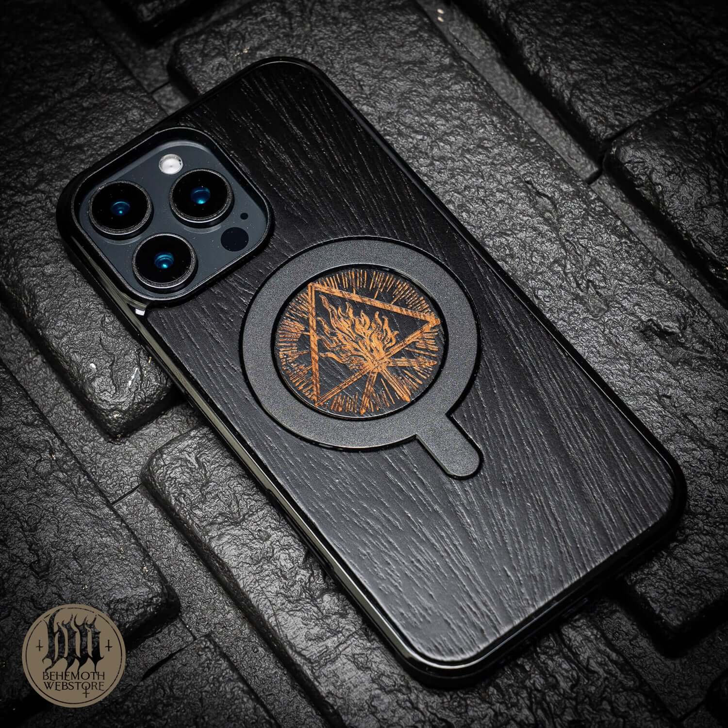 Behemoth 'Thru Fire We Walk' black oak MagSafe phone case with intricate design, made in Poland, sits elegantly on textured surface.