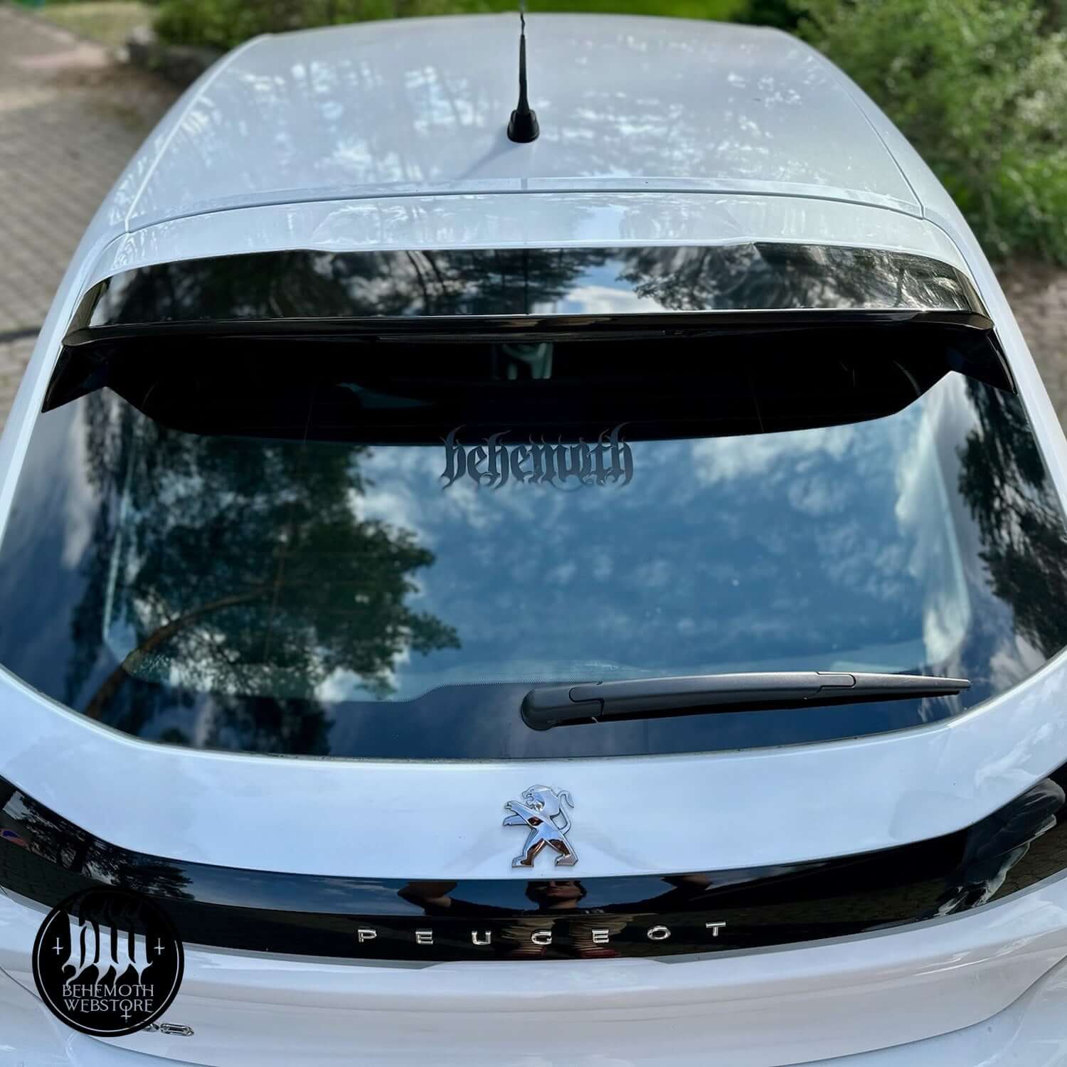 Black Behemoth logo vinyl sticker on a Peugeot car rear window, showcasing matte finish and reflective glass surface.