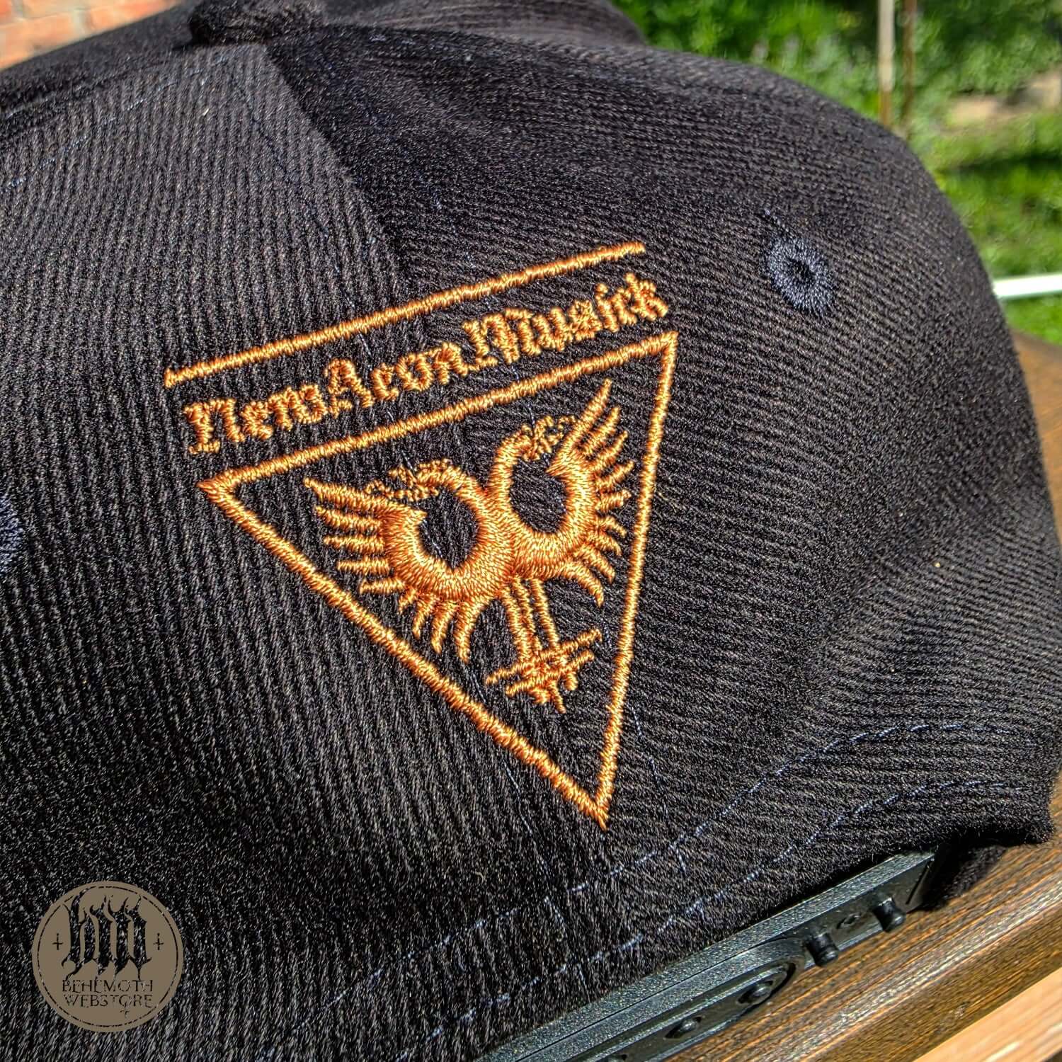 Close-up of Behemoth snapback cap with embroidered New Aeon Musick logo, featuring detailed stitching on a black fabric background.