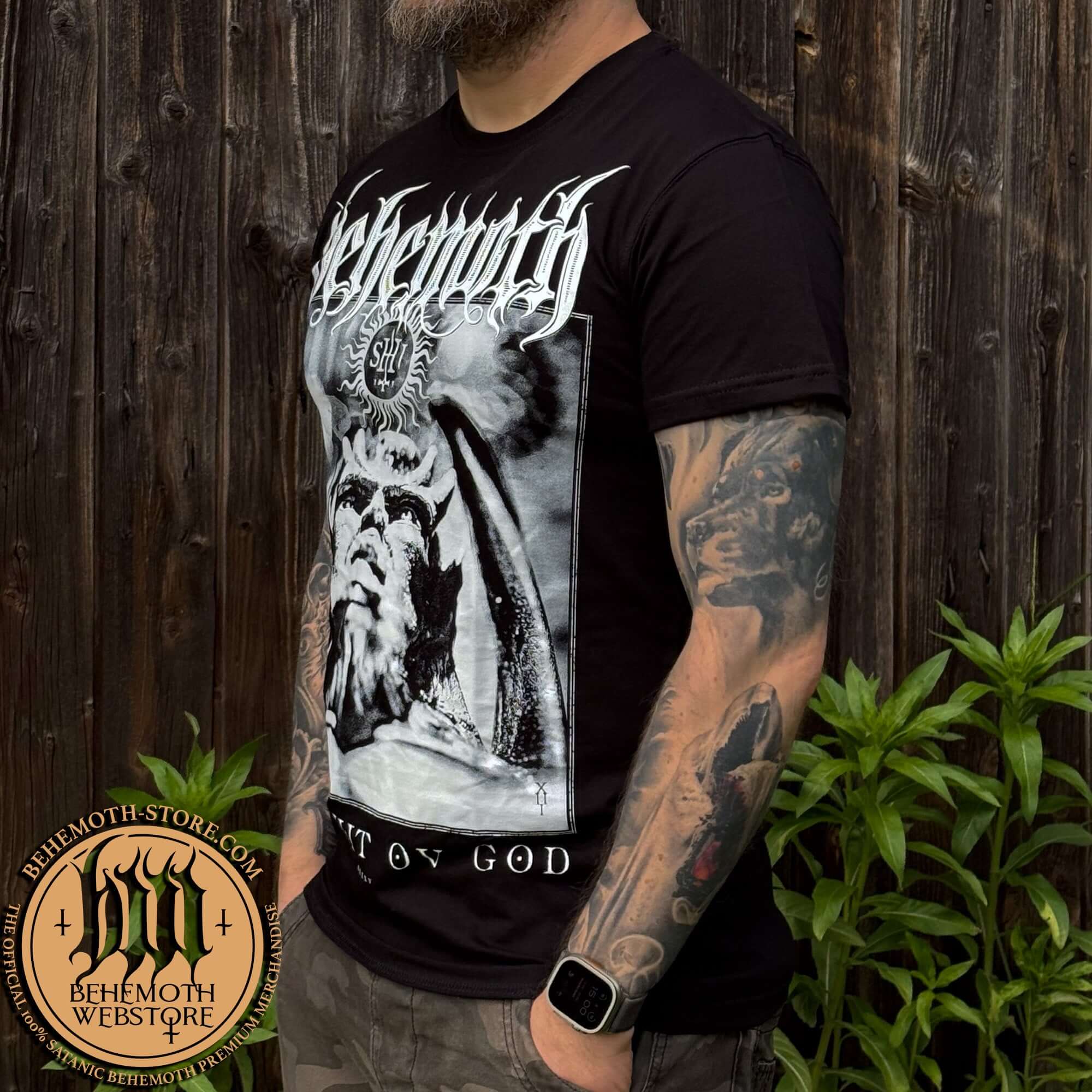 Man wearing Behemoth - The Shit Ov God t-shirt, featuring TSOG graphics, standing outdoors with tattoos visible.