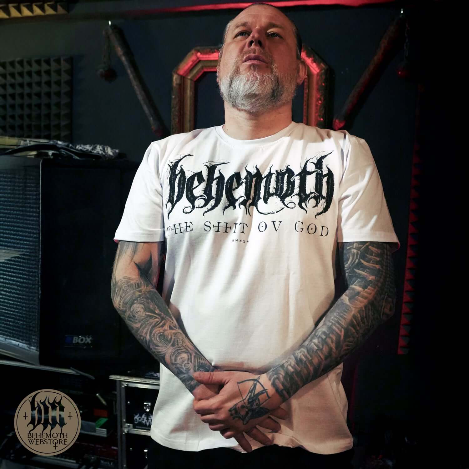 Man wearing Behemoth TSOG Sigil White T-Shirt with 'The Shit Ov God' design, showcasing iconic metal band merchandise in a music studio.