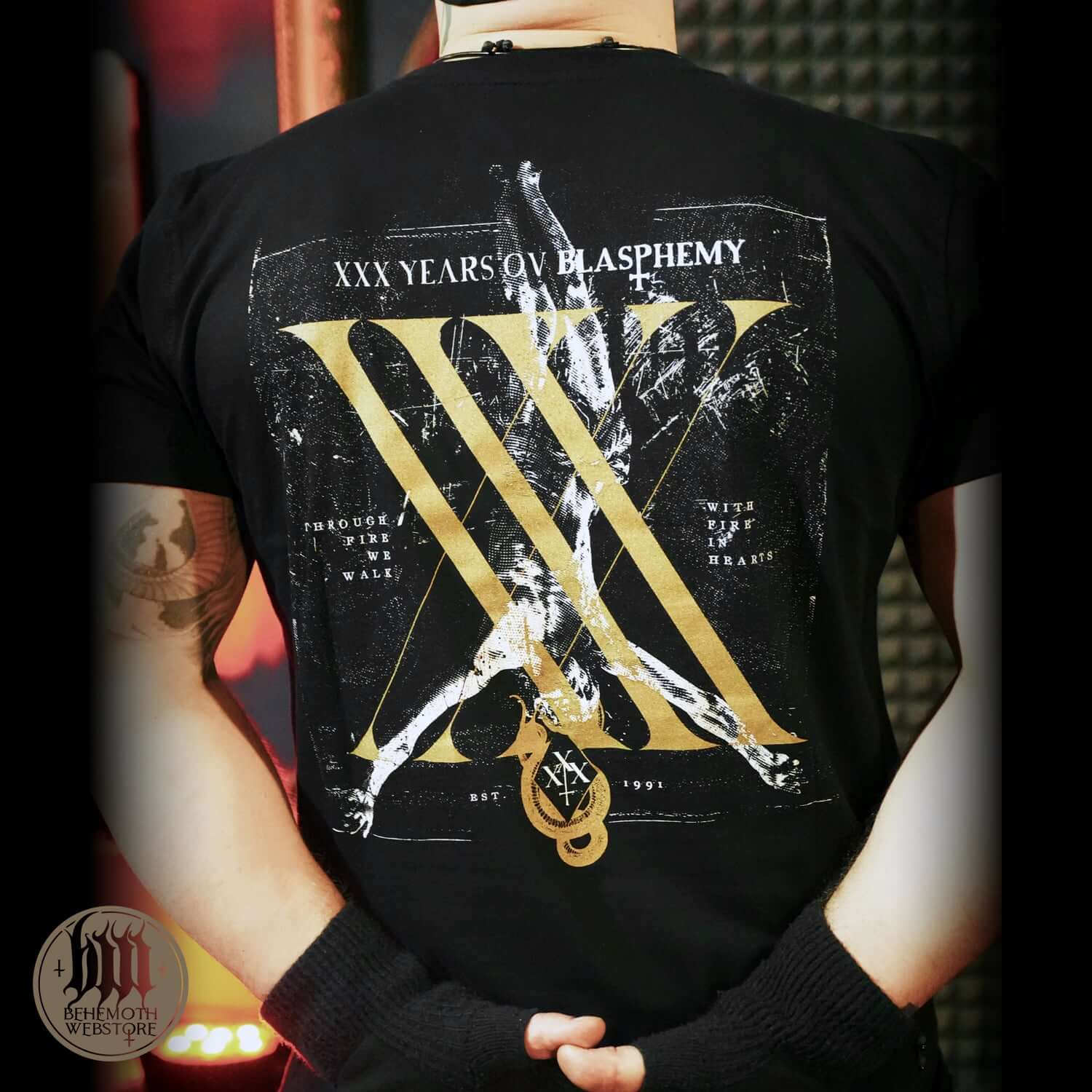 Person wearing Behemoth XXX Years Ov Blasphemy black t-shirt with iconic logo, celebrating 30th anniversary of the metal band.